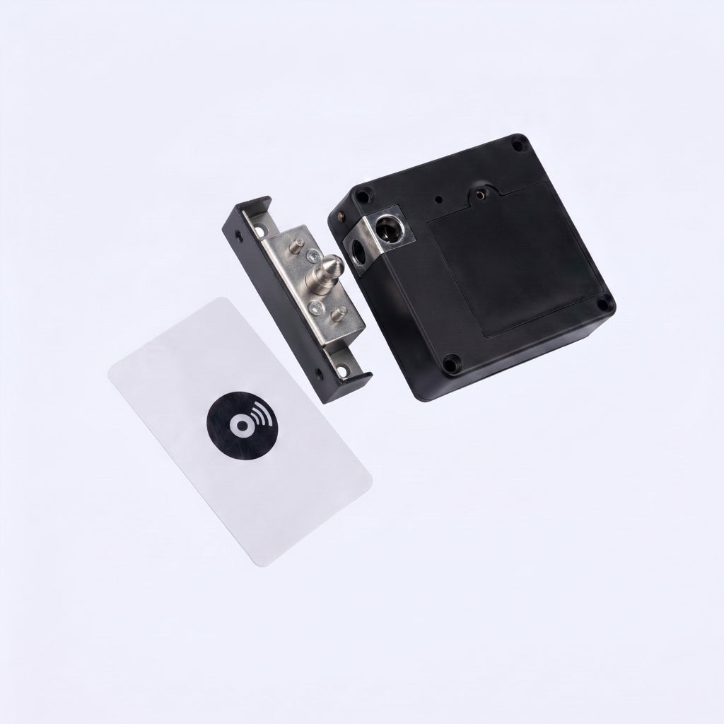 A close-up studio shot of a small electronic lock or door control component floating against a light gray background. The product appears to consist of a black rectangular housing, a silver metal latch or bracket piece, and a white rectangular card with a black circular symbol.