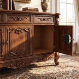 An ornate dark brown wooden credenza or sideboard cabinet with carved details, shown in a styled room with sunlight streaming in from a window. The lower right cabinet door is open, revealing a black electronic lock mechanism on the inside of the door.